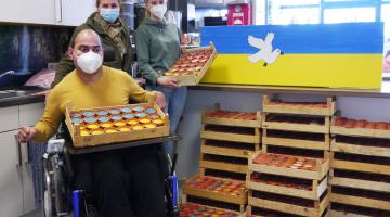 (Bild: Mitarbeiterin Marlies Knuf (Mitte) mit Beschäftigtem und Kollegin vor den verkaufsfertigen Kerzen, Kerzen auch in ukrainischen Nationalfarben erhältlich)