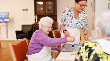 Foto: Trotz Kontaktverbot sind die Bewohnerinnen und Be- wohner der Seniorenzentren des „Pflegenetz Westmünster- land“ nicht einsam. Das gelebte Hausgemeinschaftskonzept, bzw. das Leben in kleinen Wohngruppen bietet einen festen familienähnlichen Rahmen. (Das Foto entstand vor Corona-Zeiten. Aktuell tragen alle Mitarbeiter einen Mundschutz)