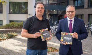 Bild: Bürgermeister Thomas Kerkhoff (rechts) und der Integrationsbeauftragte Bruno Wansing stellen das neue Kochbuch "Bocholt is(s)t bunt" vor (Copyright: Stadt Bocholt)